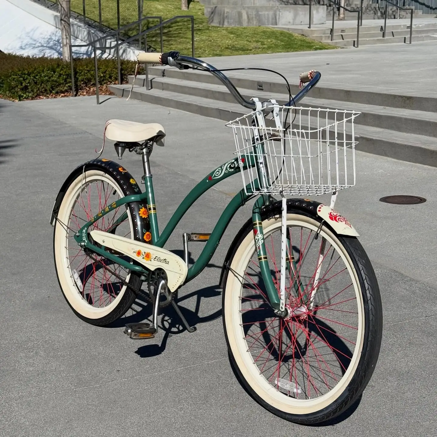 Detail of a teal cruiser fender with a hand-painted red ornamental decal and a wire basket above.